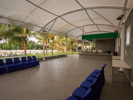 A large, empty indoor event space with a high arched ceiling, ready for setup, with rows of blue chairs stacked against a wall - Grande Bay Resort & Spa, Mamallapuram