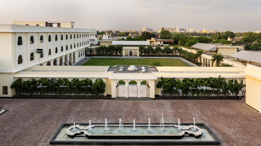 Facade of Beelwa Palace, Jaipur, featuring featuring elegant white architecture, landscaped courtyards, ornamental fountains and spacious grounds beneath an overcast evening sky