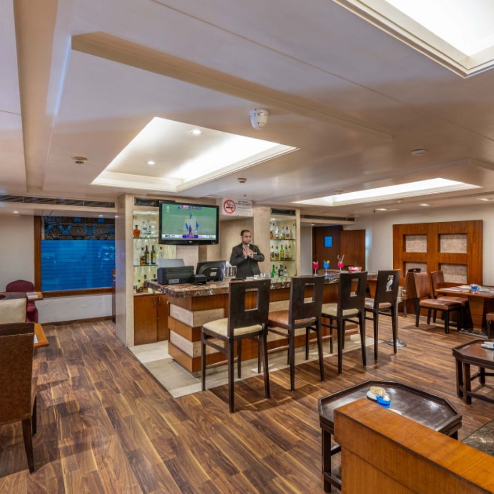 a restaurant at Libra Lords Inn Jaipur with a bar counter with high bar chairs, wall-mounted TV, and various seating arrangements 