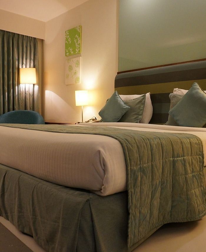 A double bed with pillows and cushions kept neatly against the head board of the bed in a warmly lit room.