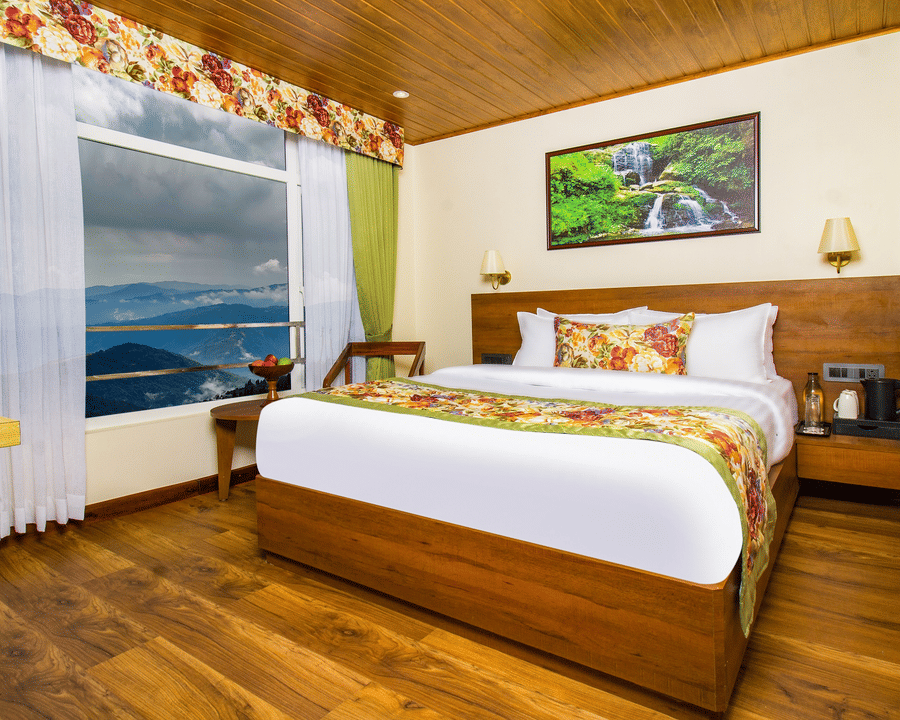 Deluxe Room featuring wooden interiors, king size bed, large window with views of hills, and cosy seating making it one of the best places to stay in Darjeeling | Mount Lungta Boutique Hotel & Spa
