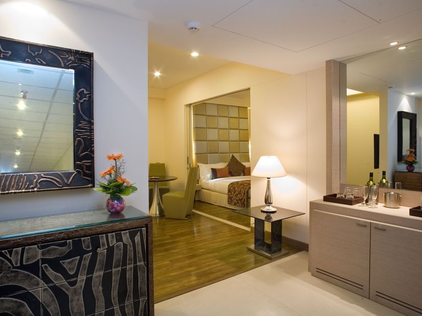 A glimpse inside a hotel room featuring a dark wood console table with a decorative mirror, a flower arrangement, and a partial view of the bed- The Sonnet, Kolkata.