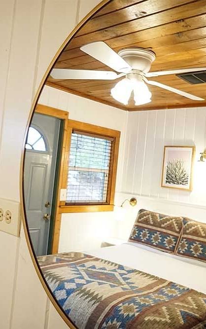 A view of a double bed in a room with wooden ceilings reflecting off a round mirror hung on the wall in front of the bed at Shaver Lake Village Hotel.