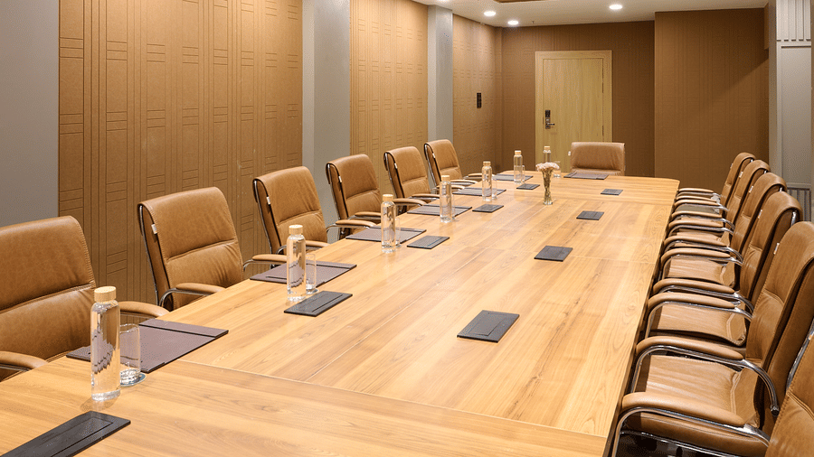A conference room featuring a long wooden table surrounded by executive chairs, wood-paneled walls, and a modern ceiling design | Voyage Eastin Suites