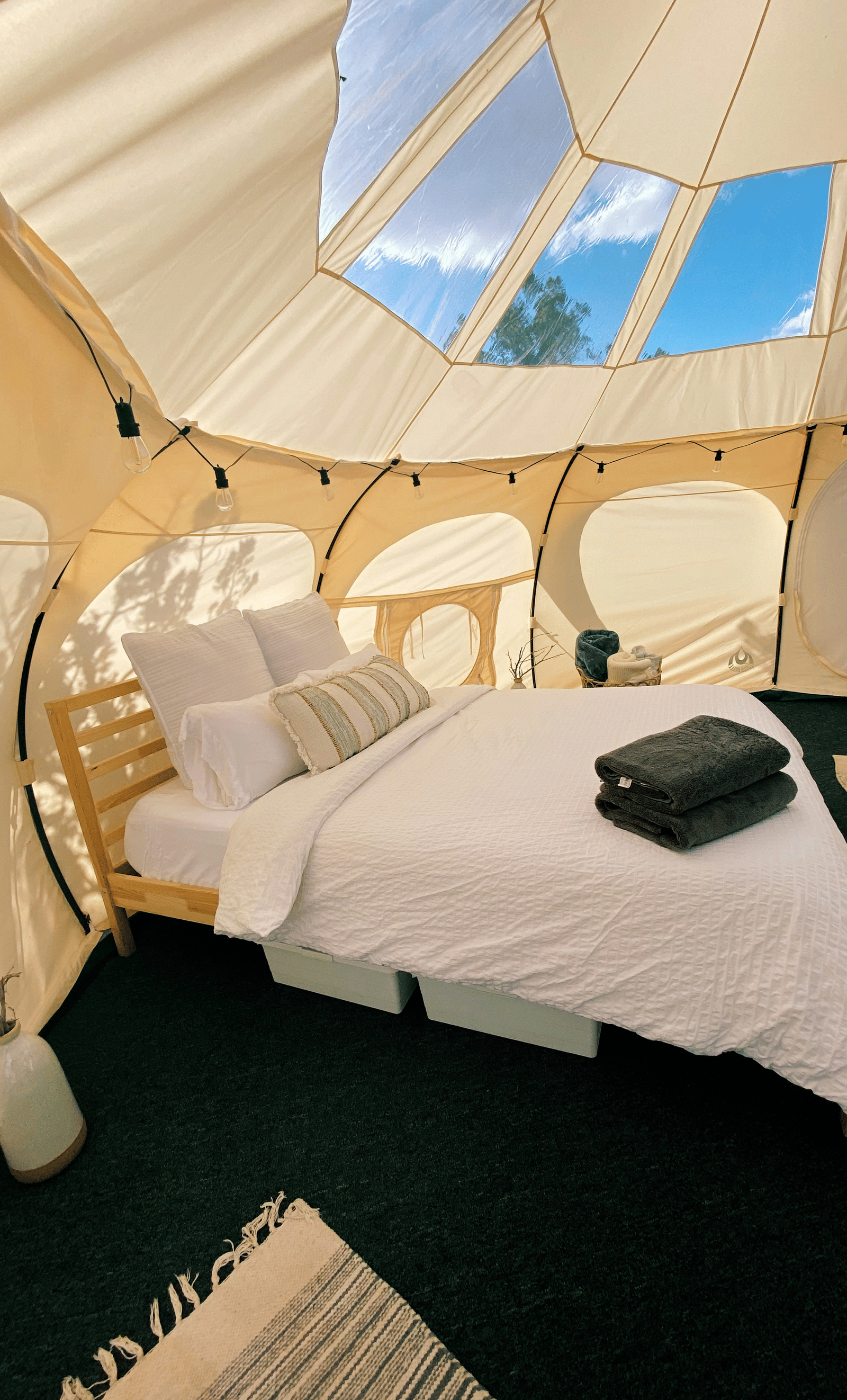 The interior of a modern glamping tent with a bed, chairs, and a window in the ceiling to view the sky.