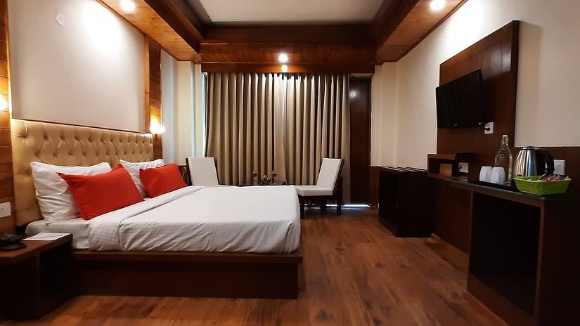 An image of a bedroom featuring a double size bed, a flat TV screen, a cabinet for storing things and a seating area at one corner - Mastiff Xanadu, Manali
