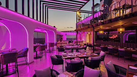 a rooftop dining area at Lords Inn Rajkot with variously arranged dining area on the floor, a balcony with seating area, and  a dimly lit ambience