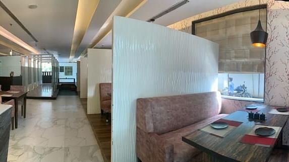 View of a restaurant with a bar counter, tables, and soft pink seating, capturing its ambience - VITS Gurugram
