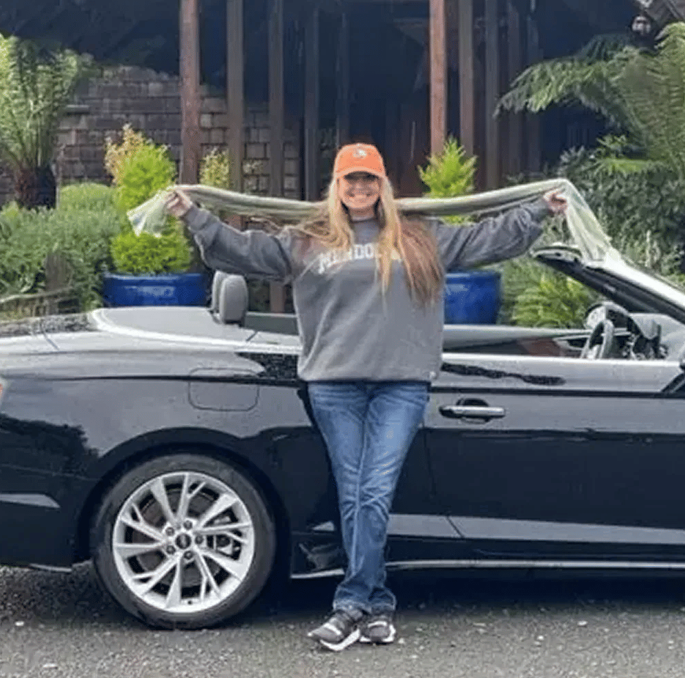 A woman posing in front of a convertible car with hand wide open holding a scarf.