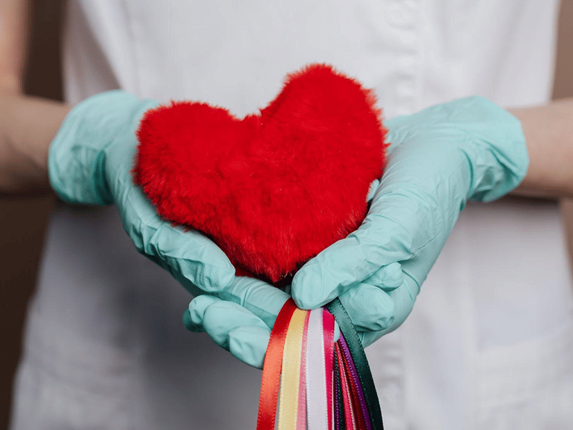 Gloved hands holding a soft red heart-shaped toy in front of a white uniform