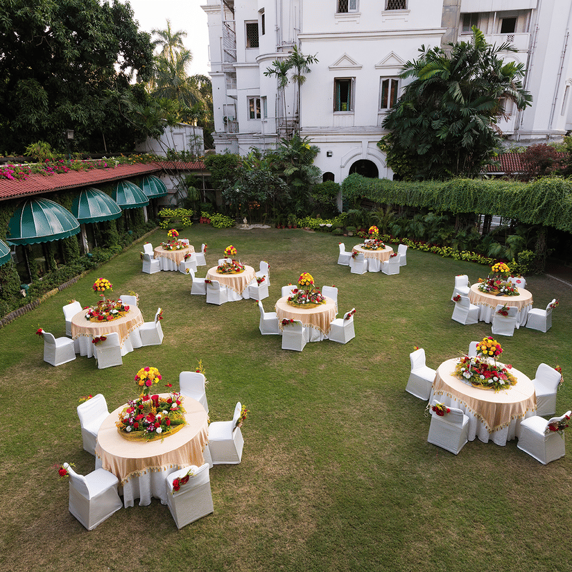 Round table seating arrangement on the lawn area at Kenilworth Hotel, Kolkata, with trees and buildings surrounding the lawn area. 