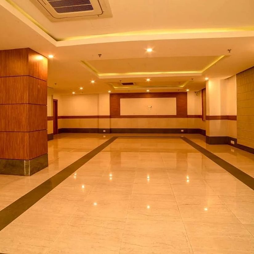 An image of a spacious banquet hall with installed lights in the ceiling - An image of a reception lobby featuring a reception desk , and a seating area for the guest - Max Hotel Prayagraj