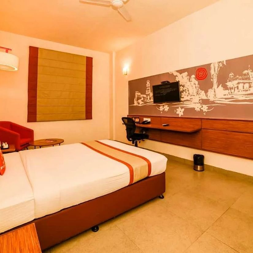 A hotel room with the bed made and pillows arranged neatly, a wall-mounted TV, and a workspace.