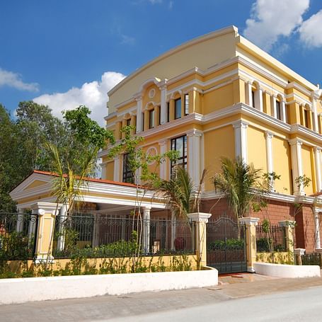An image of a hotel with an elegant entrance gate, small shrubs lining the pathway, and a lush garden in the foreground