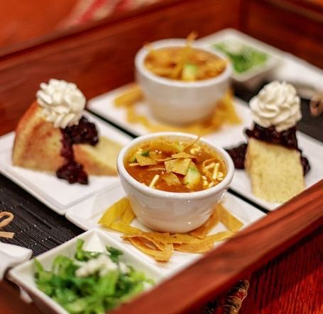 A tray of appetizers or small dishes, including dips, vegetables, and other snacks, arranged on a wooden table.