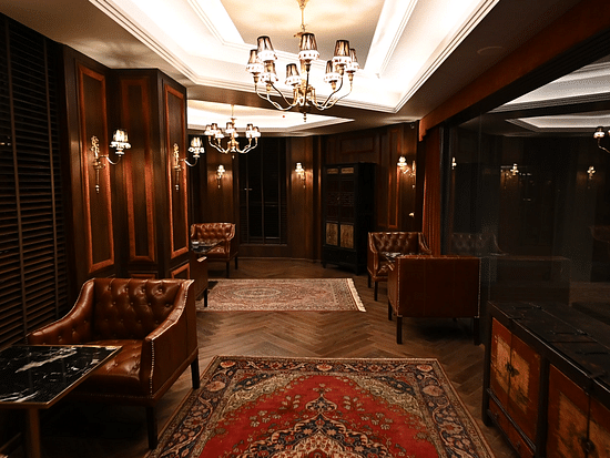 Elegant wood-panelled lounge with leather Chesterfield chairs, crystal chandeliers, and Persian rugs at The Manor Wellness & Sports Hotel