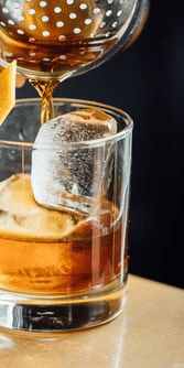 Pouring a drink into a glass with ice and an orange slice.