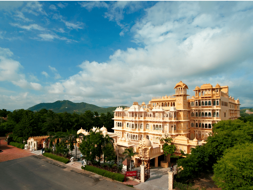 Facade of Chunda Palace next to many trees under a blue sky covered in white clouds