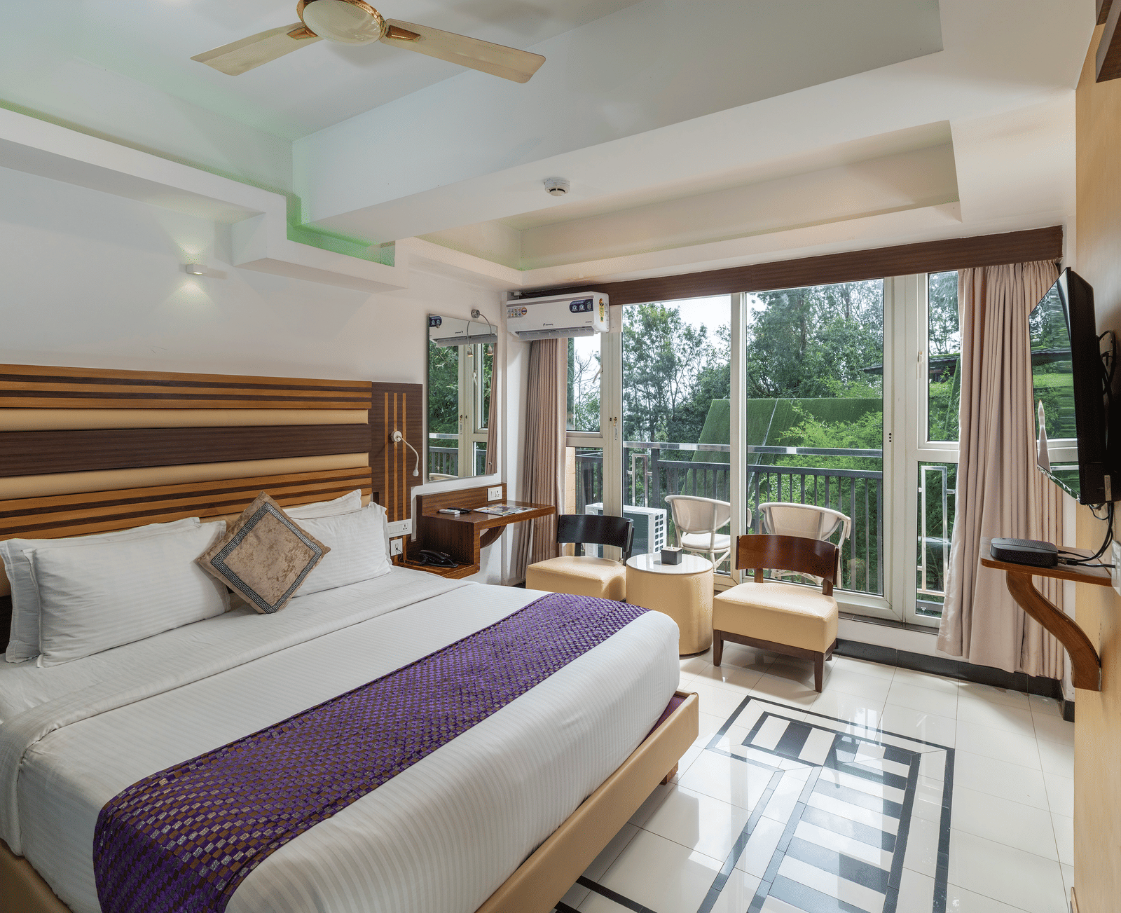 A view of Classic Non-AC room at Parakkat Nature Hotel and Resorts, Munnar featuring a large bed, light wood furnishings, a ceiling fan, and a balcony with an outdoor greenery view.