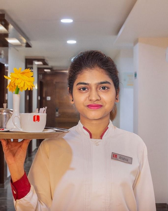 A smiling hotel staff member at Lords Inn Porbandar, carries a tray with beverages in a brightly lit area.