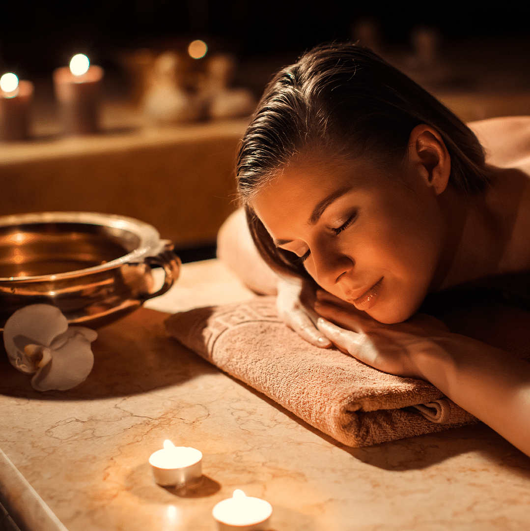 Woman relaxing during a spa treatment surrounded by candles, enjoying a moment of calm
