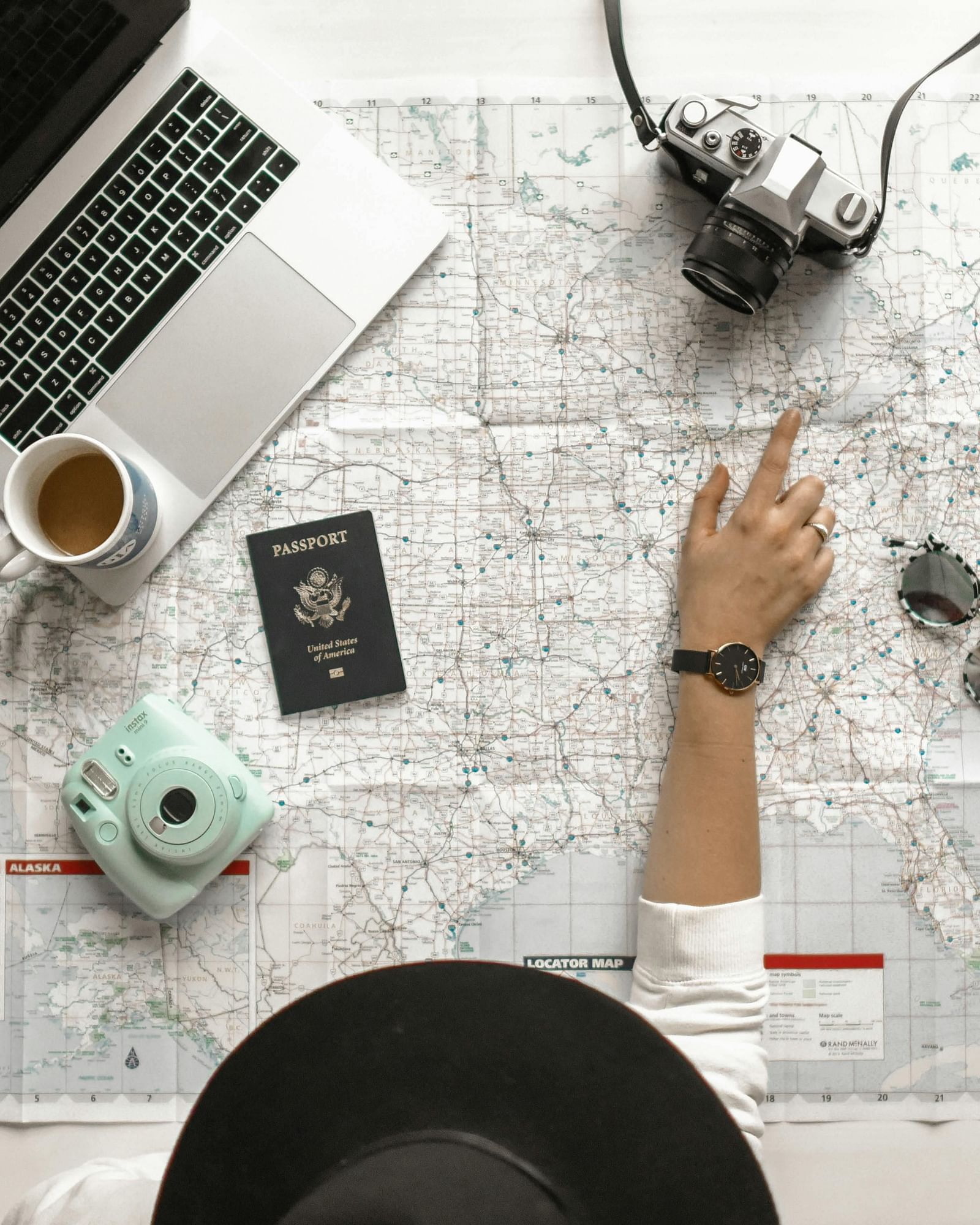 An overhead shot of a person working with a laptop, camera, phone, and travel documents placed over a huge map.
