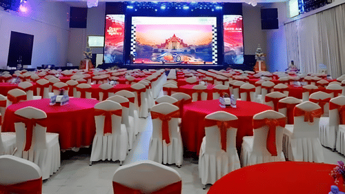 WhatsApp Image 2025-03-Banquet hall with red and white table settings and a large LED screen at Central Hotels.17 at 16.38.37