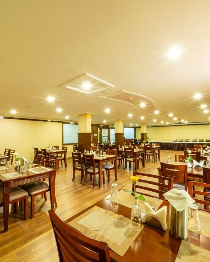 A brightly lit dining room with wooden tables and chairs offers a welcoming atmosphere for meals at Lords Midtown Suites.