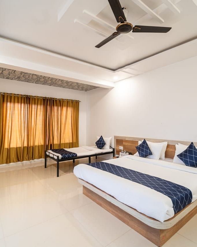 Penthouse Suite with Balcony featuring a king size bed with white linens and a gray accent runner, two blue decorative pillows, bedside tables, a mattress, and a ceiling fan.