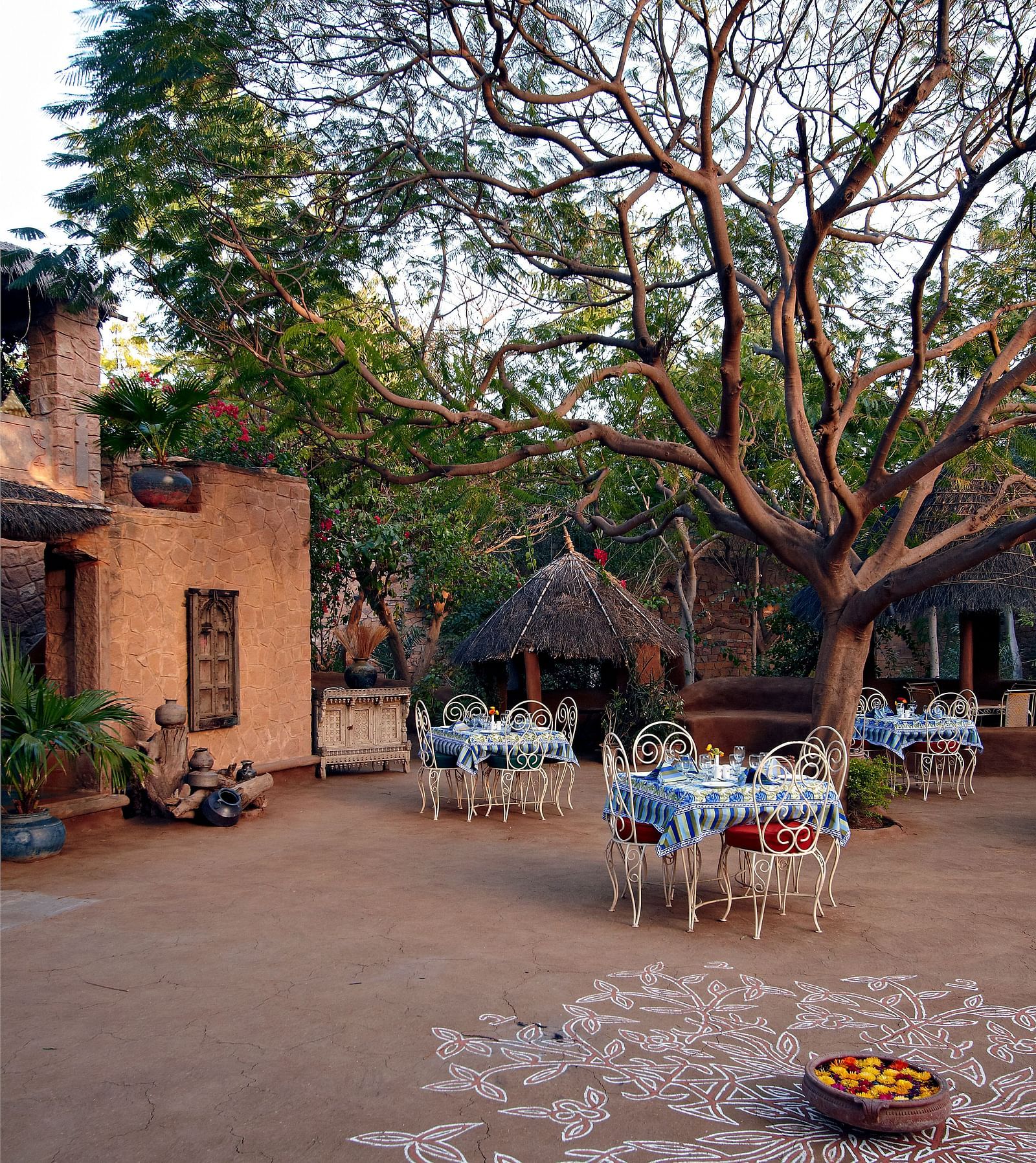 An image of the outdoor seating arrangement of the Taasli Restaurant at Manvar Shergarh with greenery around - Manvar Resort & Desert Camp