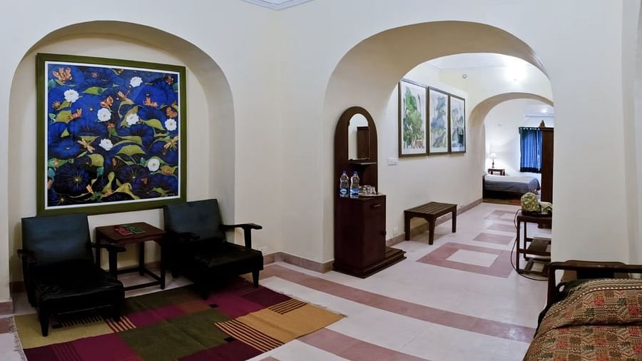 Hallway with arched doorways, artwork, armchairs, rug, patterned floor tiles, furniture, and a distant bed - Tijara Fort-Palace - 19th Century, Alwar.