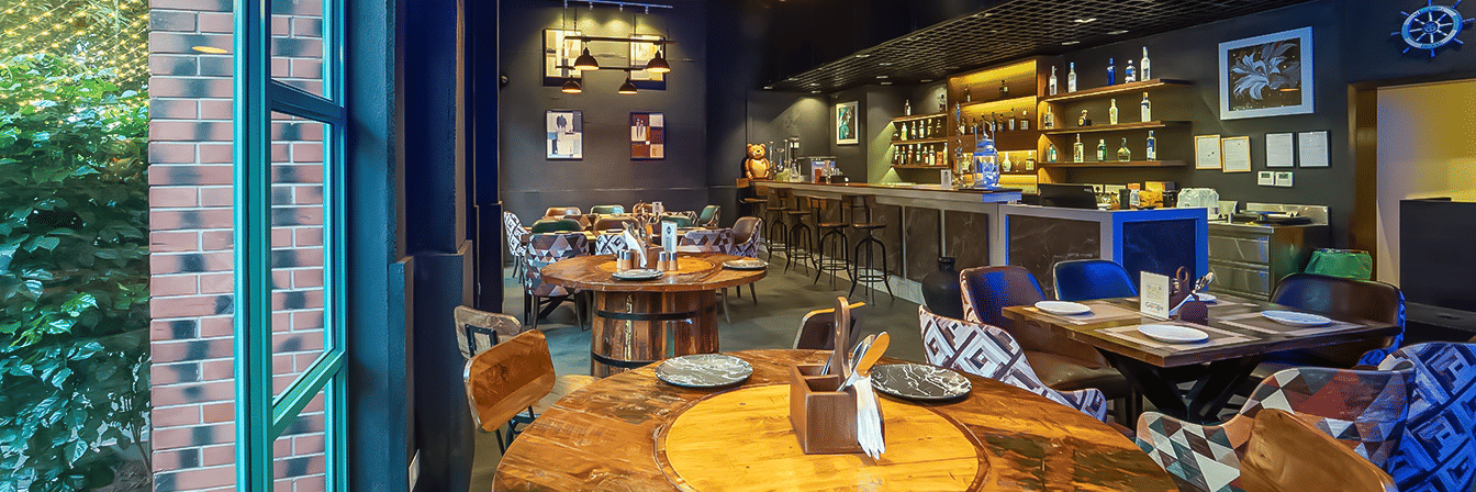 Moody restaurant interior with rustic wooden tables, eclectic chairs, and a backlit bar with liquor shelves