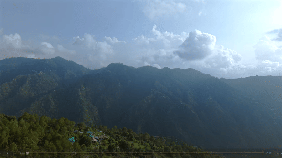 Sweeping view of the lush green hills and distant mountains under a clear blue sky with scattered clouds, capturing the natural beauty of Shimla.