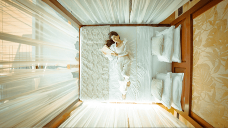 A person lying on a large white bed draped with sheer white fabric in a room with warm lighting at Amanzi Resort.