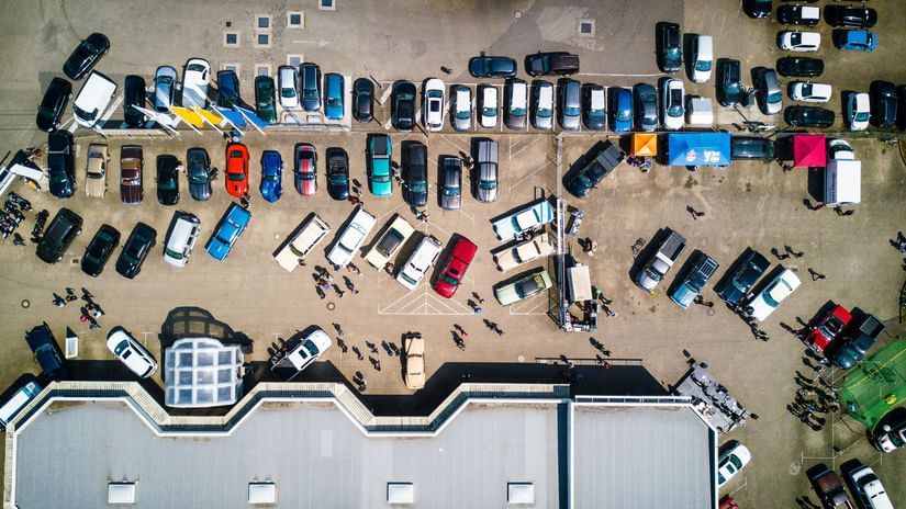 An aerial view of a parking lot full of vehicles besides a large building.
