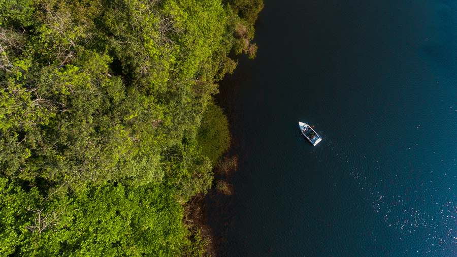 An aerial view shows a lake with a boat, surrounded by green cliffs.