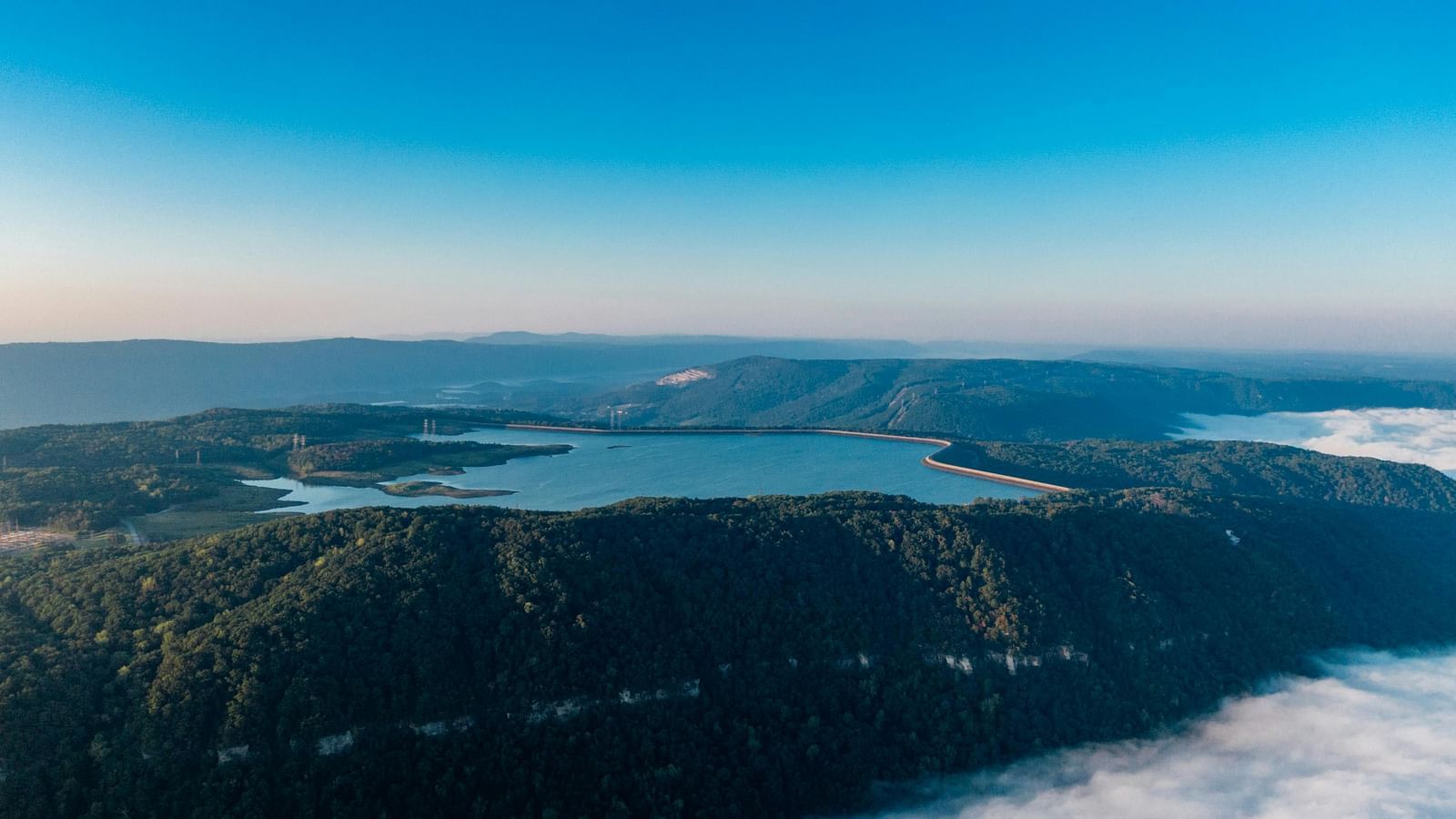 an Ariel view of a damn filled with blue water with trees covering the entire waterbody.