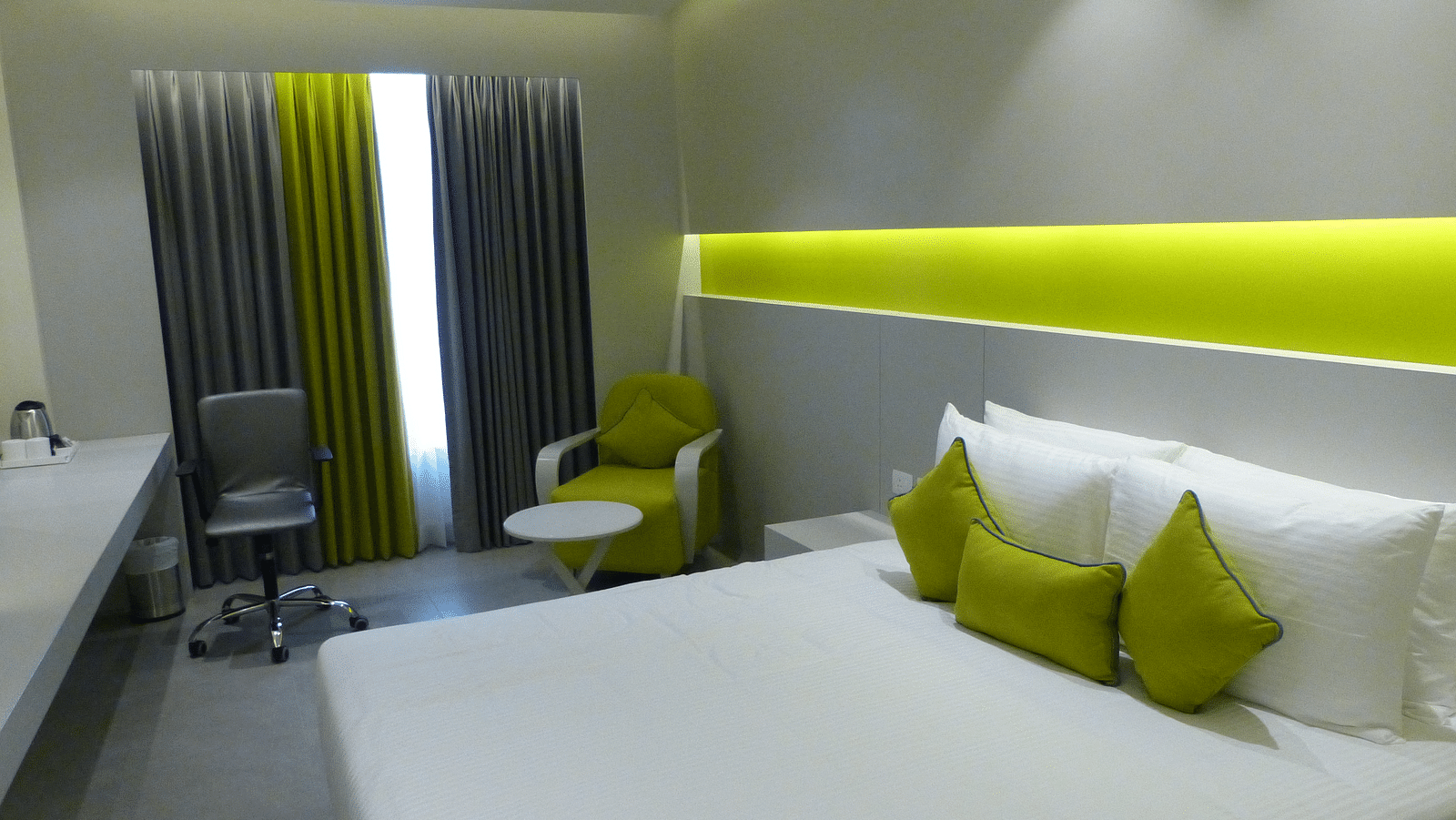  Spacious twin beds with headboards line the wall, large windows with curtains cover them, and a sofa is placed near the window