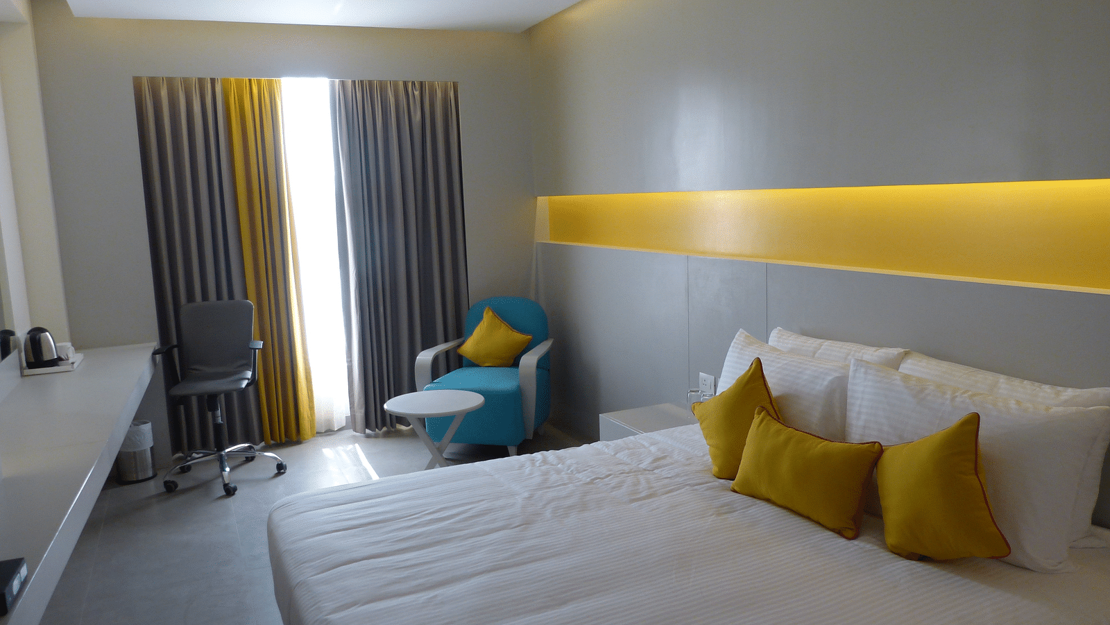  Spacious twin beds with headboards line the wall, large windows with curtains cover them, and a sofa is placed near the window