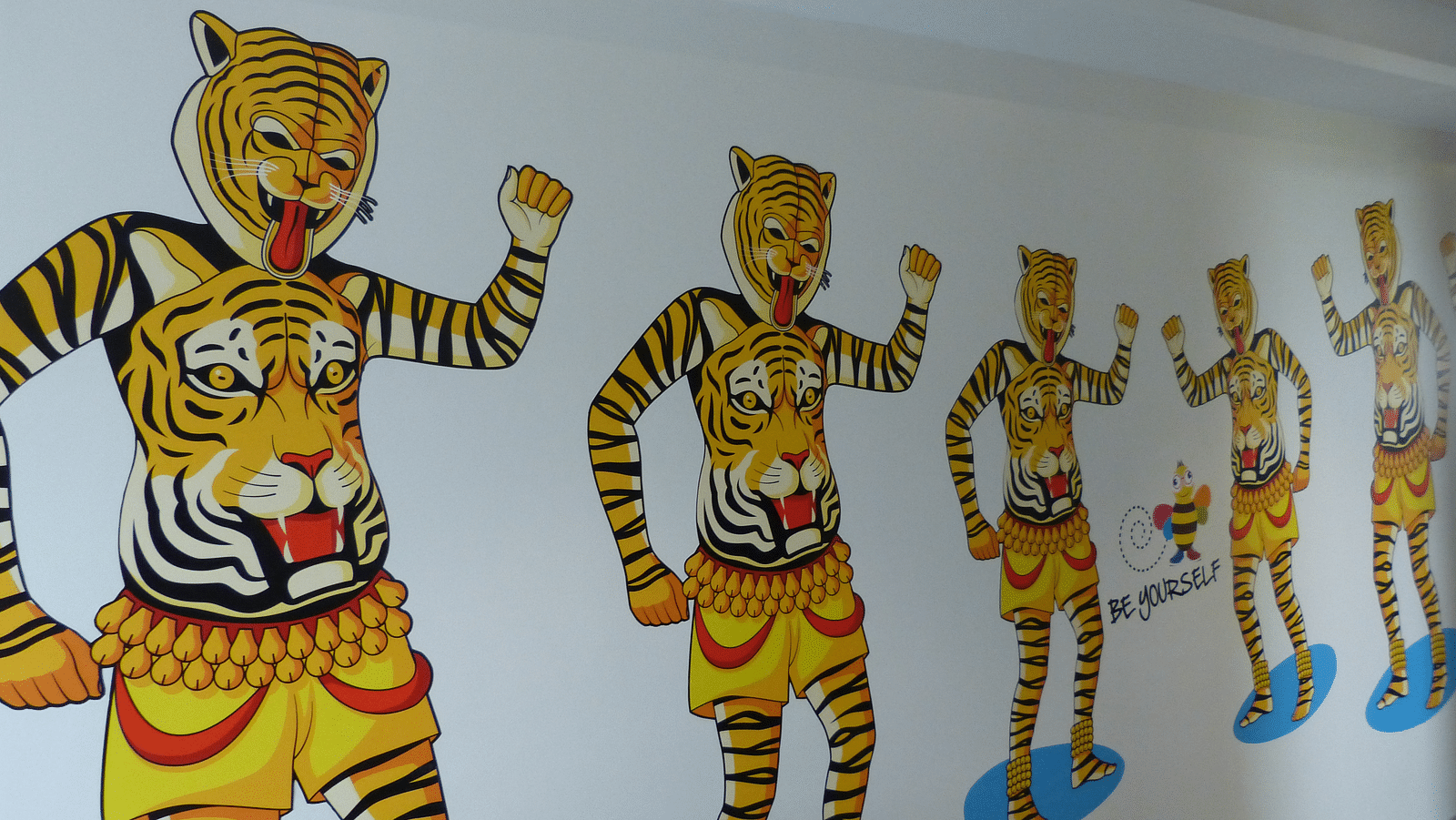 People dressed as tigers, with their bodies painted in vibrant colours, are shown on the wall