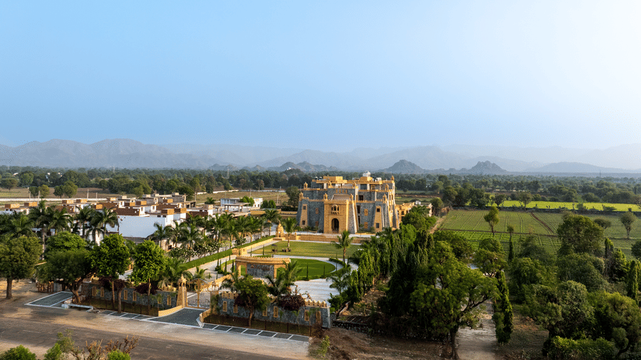 An aerial view of the EsthereaRaj Leela, Ranakpur, nestled within a lush green landscape and distant hills.
