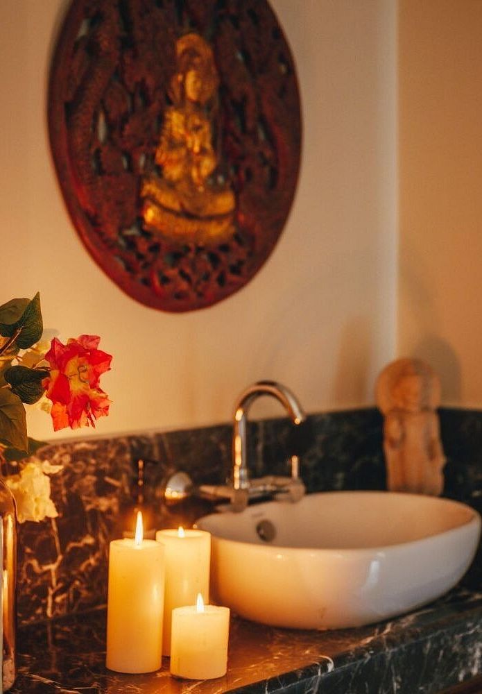 Wash basin with lit candles and a Buddha wall hanging above, placed in a softly lit space at Karma Chalets.