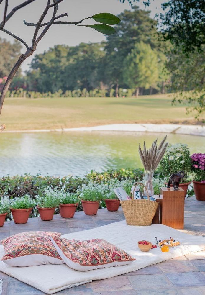 Table setup by the lake at Karma Chalets with potted plants, some food items, and outdoor scenery in the background.