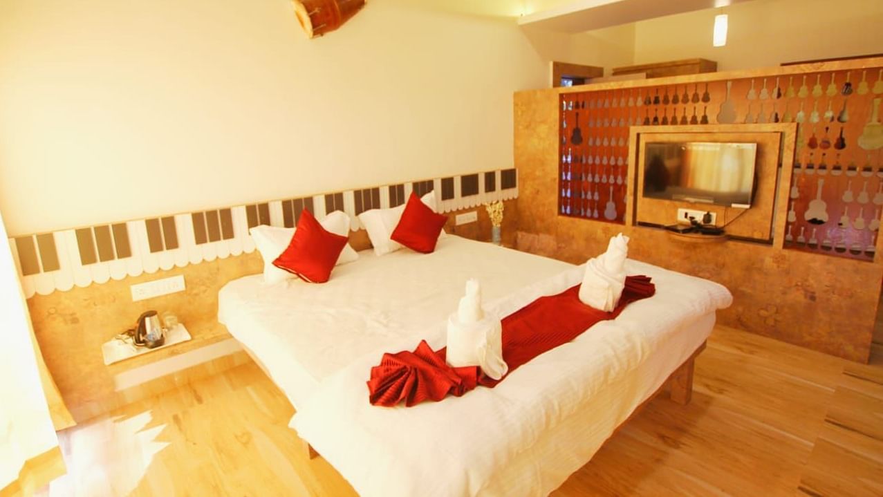 A diagonal view of the room featuring a spacious bed with towels folded in different shapes on it. There is a wooden table with a wall-mounted television at SeaFort Beach Resort