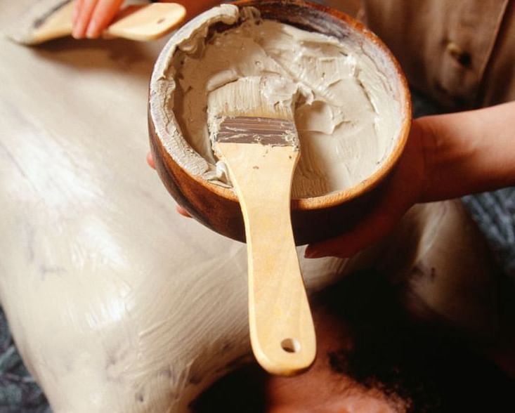 Ayurvedic spa treatment in progress, with a wooden bowl pouring herbal oil or buttermilk onto a person's forehead.