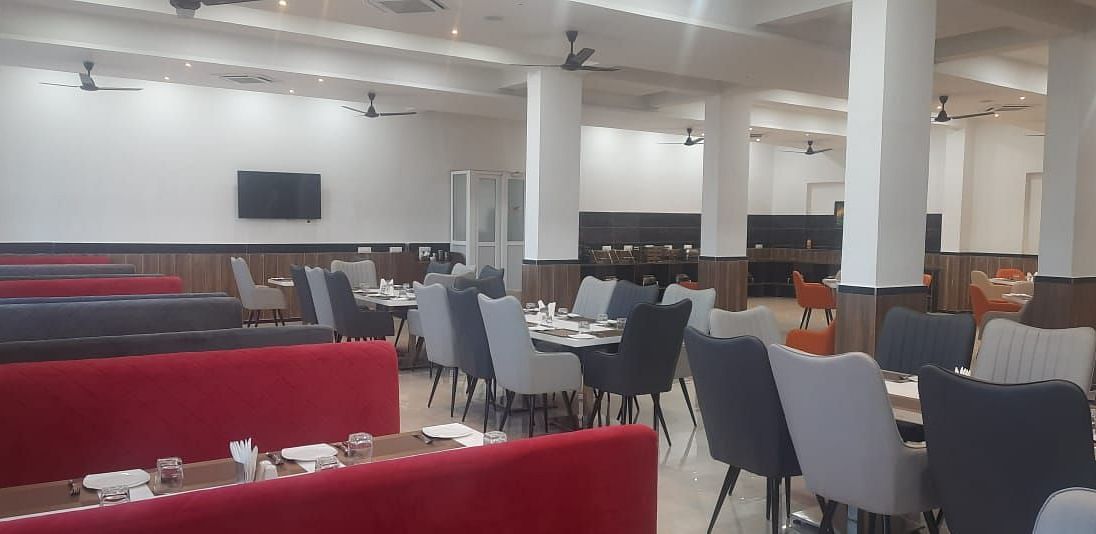 A brightly lit dining area features tables with red bench seating and grey chairs - Kankidham Lords Inn