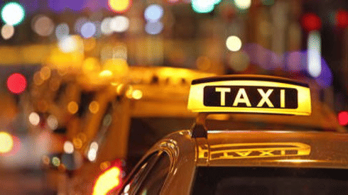 close up image of the taxi signage glowing during the night put above yellow coloured taxis