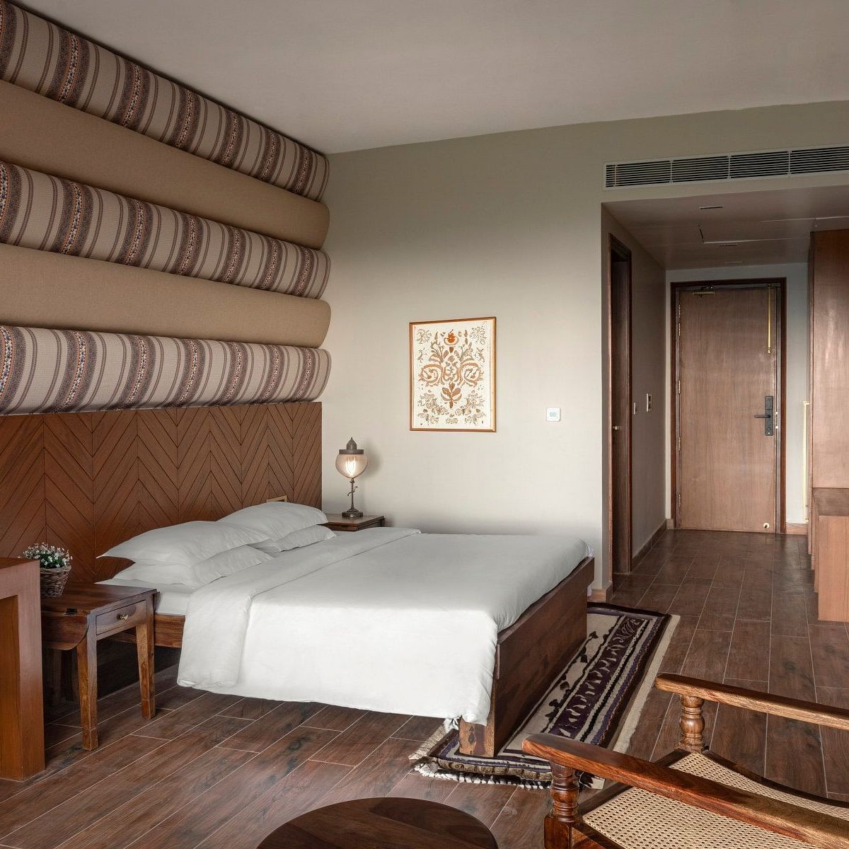 An elegantly designed room with patterned fabric wall decor above the bed, wooden furniture, and a comfortable seating area - The Samai, Bhimtal