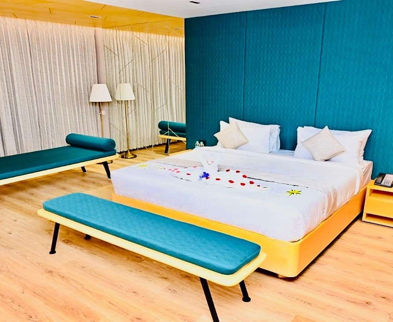 Close up view of a Presedential Suite featuring a King size bed with white linens and decorative swans, a green accent wall, yellow furniture, and hardwood floors - Dhanalakshmi Srinivasan Hotels, Perambalur
