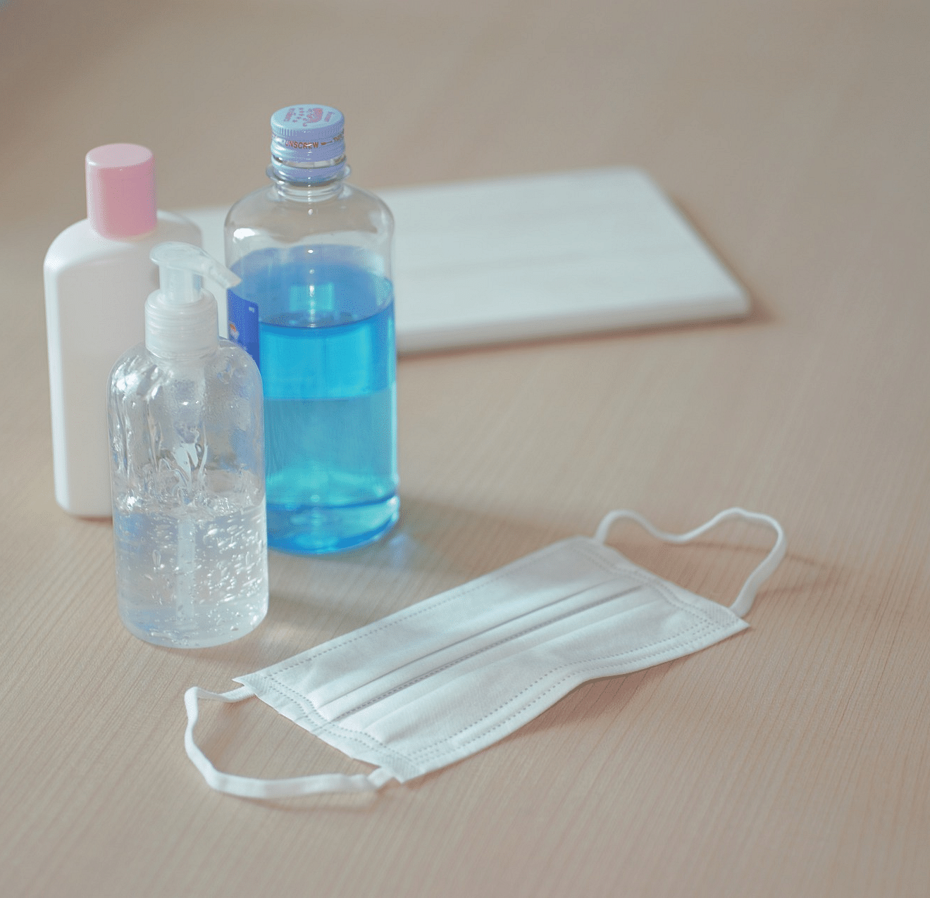 An image of sanitary products on the floor, including a face mask, towel, and sanitizers.